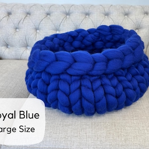 May include: A large, round, royal blue basket crafted from thick, chunky knit yarn. The basket features a prominent braided texture throughout its circular structure. A white label in the corner displays the text Royal Blue Large Size.