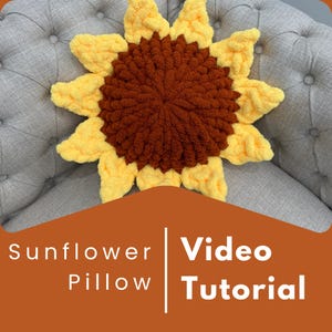 Può includere: Un cuscino a forma di girasole fatto a mano, con un centro marrone e petali gialli. Il cuscino è realizzato in filato morbido e strutturato e ha la forma di un girasole. Il testo "Sunflower Pillow Video Tutorial" è visualizzato su sfondo arancione.