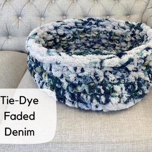 Puede incluir: Una cesta redonda te&ntilde;ida con efecto tie-dye en color denim descolorido. La cesta est&aacute; hecha de un material suave y afelpado en tonos azules, blancos y verdes. El texto "Tie-Dye Faded Denim" est&aacute; en una etiqueta blanca.