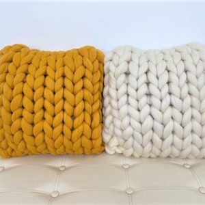 May include: Two chunky knit throw pillows, one mustard yellow and one white, on a white tufted couch.