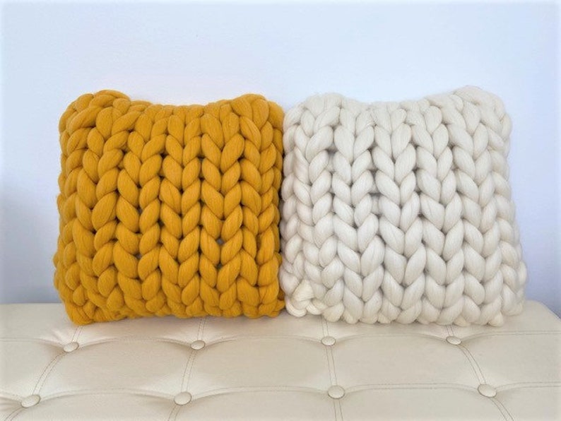 May include: Two chunky knit throw pillows, one mustard yellow and one white, on a white tufted couch.