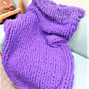 May include: A large, purple, chunky knit throw blanket is draped over a couch.