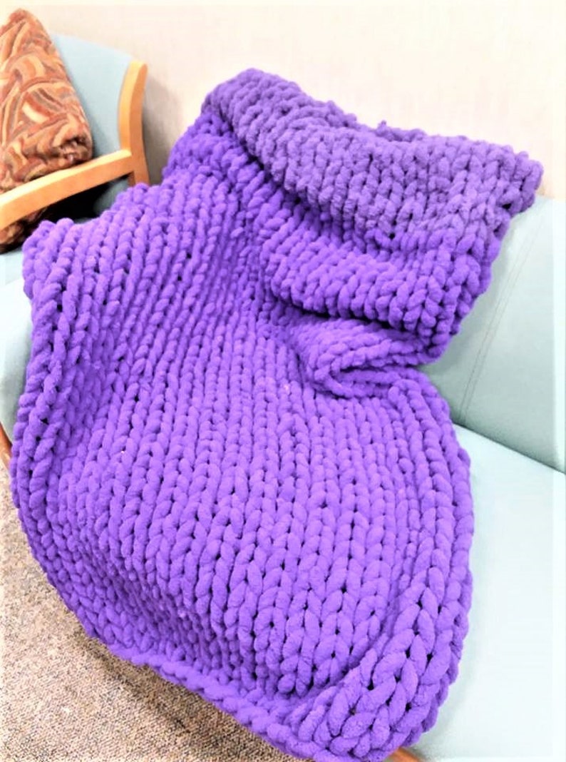 May include: A large, purple, chunky knit throw blanket is draped over a couch.