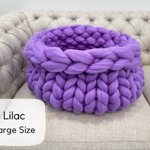 May include: A large, round, chunky knit basket made of thick, soft lilac yarn. The basket features a prominent braided texture throughout its structure, with a wide, open top and a deep, hollow interior. The text 'Lilac Large Size' is visible.