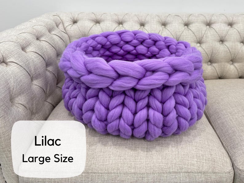 May include: A large, round, chunky knit basket made of thick, soft lilac yarn. The basket features a prominent braided texture throughout its structure, with a wide, open top and a deep, hollow interior. The text 'Lilac Large Size' is visible.