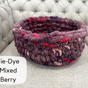 Puede incluir: Una cesta redonda te&ntilde;ida con tinte anudado en colores de bayas mixtas, que incluyen tonos de morado, rosa y rojo. La cesta est&aacute; hecha de un hilo grueso y texturizado y se encuentra sobre una superficie tapizada gris. El texto "Tie-Dye Mixed Berry" est&aacute; en un cuadro blanco.