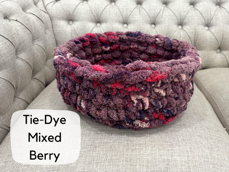 Puede incluir: Una cesta redonda te&ntilde;ida con tinte anudado en colores de bayas mixtas, que incluyen tonos de morado, rosa y rojo. La cesta est&aacute; hecha de un hilo grueso y texturizado y se encuentra sobre una superficie tapizada gris. El texto "Tie-Dye Mixed Berry" est&aacute; en un cuadro blanco.