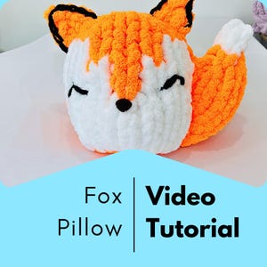 Op de afbeelding: Een handgemaakt vossen-vormig kussen in oranje, wit en zwart. Het kussen heeft een zachte textuur en een lachend gezicht met gesloten ogen. De tekst "Fox Pillow Video Tutorial" wordt weergegeven op een blauwe achtergrond.