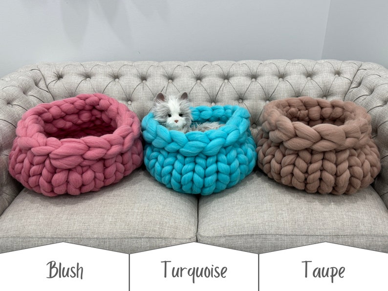 May include: Three round, chunky knit pet beds in blush, turquoise, and taupe. The turquoise bed contains a small, fluffy, grey and white plush cat toy. Each bed features a thick, braided yarn construction with a deep, circular opening.