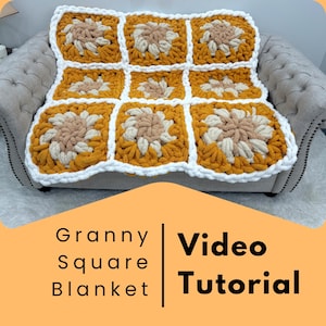 Peut inclure: Une couverture granny square faite à la main, aux tons jaune moutarde, crème et beige, drapée sur un canapé gris. La couverture présente un motif floral avec des bordures blanches. L'image comprend le texte "Granny Square Blanket | Video Tutorial".