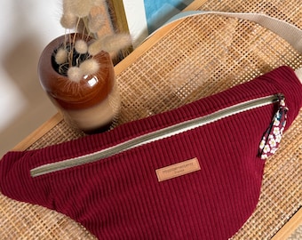 May include: A burgundy corduroy fanny pack with a cream strap and a floral zipper pull. The bag has a zip closure and a small leather tag that reads "Missbertaberry France".