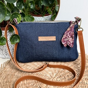 Op de afbeelding: Een donkerblauwe crossbody tas met een bruine leren riem en een decoratieve bloemen sjaal. De tas heeft een ritssluiting en een klein rechthoekig label met de tekst "Missliberteliberty France".