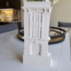 May include: A white architectural model of a building with a detailed facade, including a window, columns, and a decorative arched doorway. The base of the model has text that reads "U.S. Municipal Building, New York City, 1903."