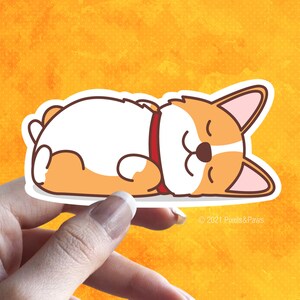 May include: A cartoon illustration of a sleeping corgi dog with a red collar. The dog is lying on its back with its paws in the air. The background is a yellow watercolour wash.