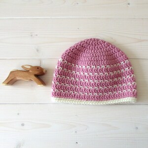 May include: A pink and white striped crocheted beanie hat with a white crocheted brim.