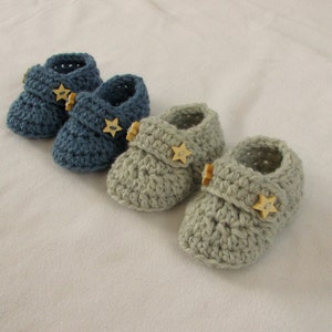 Könnte beinhalten: Zwei Paar gehäkelte Babyschuhe mit sternförmigen Knöpfen. Ein Paar ist blau und das andere grau.