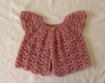 Op de afbeelding: Een roze gebreid babyvest met een hartvormige knoop.