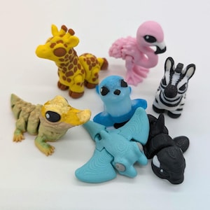 May include: A collection of colorful animal figurines, including a yellow giraffe with brown spots, a pink flamingo, a zebra with black and white stripes, a blue seal, a light blue pterodactyl, a green alligator, and a black orca.
