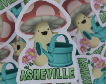 May include: A white mushroom with a red and white cap holding a blue watering can. The mushroom is smiling and has a green leaf on its head. The text "ASHEVILLE" is written in green letters below the mushroom.