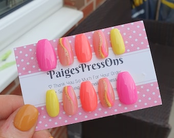 Puede incluir: Un conjunto de 7 uñas postizas de color rosa, amarillo y melocotón con detalles de purpurina dorada. Las uñas están dispuestas en una tarjeta de lunares rosa y blanca con el texto "Paiges PressOns" y "Thank You So Much For Your Order".