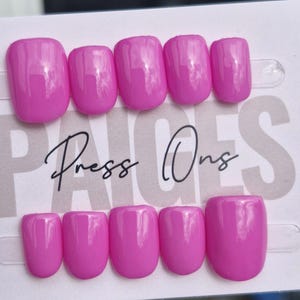 May include: A set of ten glossy, solid hot pink press-on nails arranged in two rows on a white display card. The card features the text PAIGES Press Ons in black and grey lettering. Each nail has a smooth, rounded square shape and a vibrant finish.