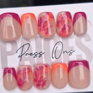 May include: A collection of press-on nails with diverse designs. Some nails have a nude base with a magenta tip, others have an orange tip. Several nails feature a pink and red marbled design with glitter.