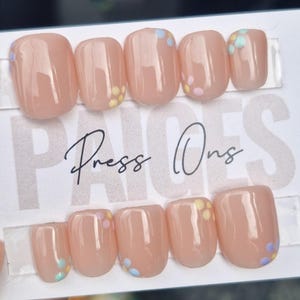 May include: A set of ten nude press-on nails with a floral design. The nails have a light pink base with small, colourful flowers on each nail.