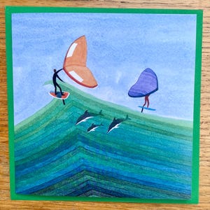 Może przedstawiać: Akwarelowa ilustracja dwóch postaci uprawiających windsurfing z kolorowymi żaglami nad zielono-niebieskim oceanem. Poniżej powierzchni pływają delfiny. Grafika osadzona jest na tle jasnoniebieskiego nieba i obramowana zieloną obwódką.
