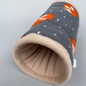 Peut inclure: Un tunnel pour animaux de compagnie en polaire gris et orange avec un motif de pois blancs. Le tunnel est fait d'un tissu doux et pelucheux et a une doublure beige. Le tunnel est conçu pour que les petits animaux de compagnie puissent jouer et explorer.