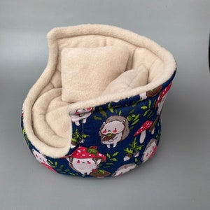 May include: A blue and white hedgehog-themed pet bed with a removable cream-colored cushion. The bed is made of soft fabric and has a rounded shape.