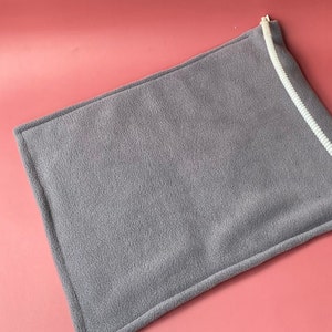 May include: A grey fleece heating pad with a white cord attached. The pad is designed to provide warmth and comfort.