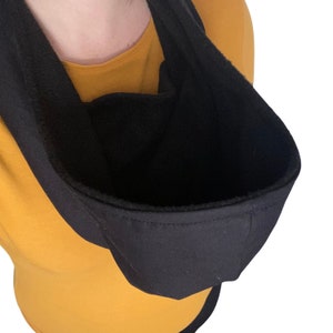 May include: A black hooded sweatshirt with the hood pulled up and turned inside out, showing the soft fleece lining. The sweatshirt is worn over a yellow shirt.