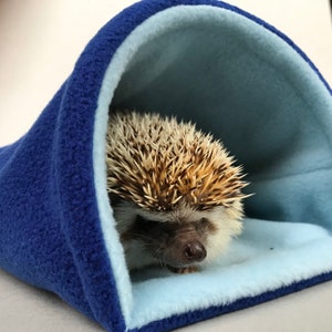 May include: A blue and light blue fleece hedgehog sleeping bag. The sleeping bag is designed to provide a cozy and safe space for a hedgehog to sleep.