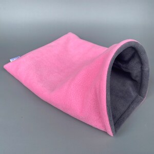 May include: Pink and gray fleece pet bed shaped like a tunnel. The bed is made of soft, plush fleece and has a cozy, enclosed design.