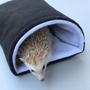 May include: A small hedgehog is curled up inside a black and white fleece sleeping bag. The sleeping bag is designed to provide a cozy and safe space for the hedgehog to rest.