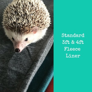 May include: A small hedgehog curled up on a grey fleece liner. The liner is part of a larger bedding set for small animals. The text on the right side of the image reads "Standard 3ft & 4ft Fleece Liner".