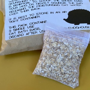 May include: A white mesh bag filled with oatmeal flakes. The bag is labeled "This pack contains 5 single use oat bath bags, discard after use".