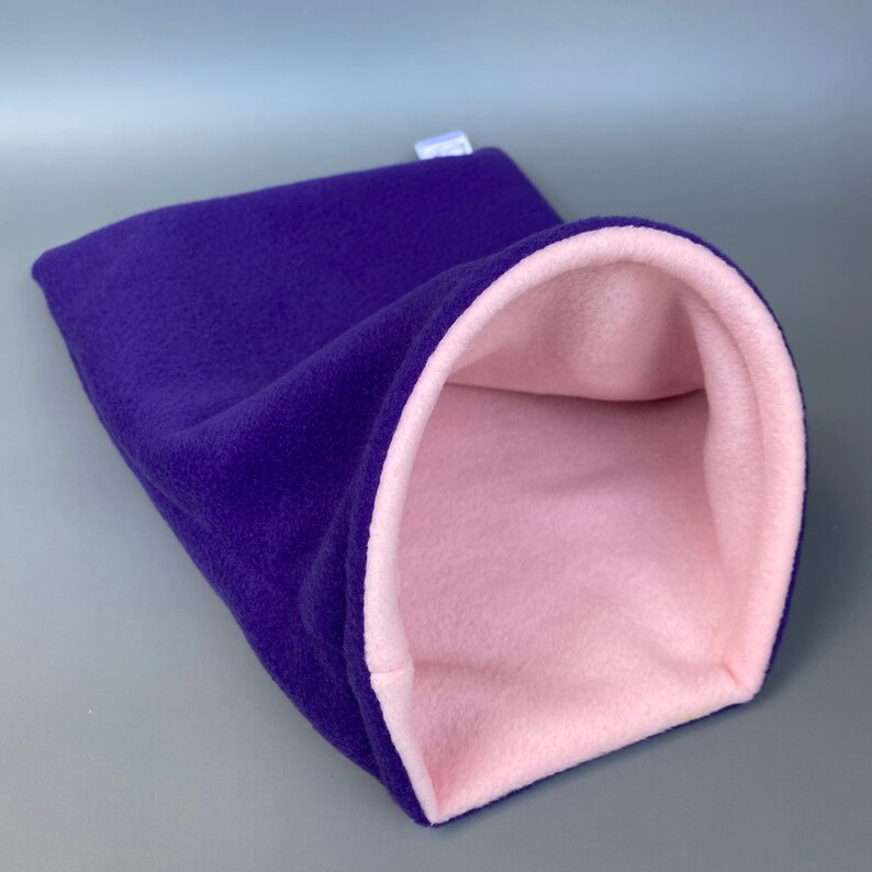 May include: Purple and pink fleece pet bed shaped like a tunnel. The bed is made of soft, cozy fleece and is perfect for small animals like hamsters, gerbils, or rats.
