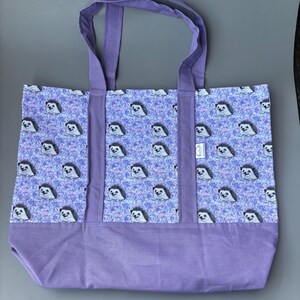 K&ouml;nnte beinhalten: Eine lilafarbene Einkaufstasche mit einem Muster aus Igeln auf helllilafarbenem Hintergrund. Die Tasche hat zwei lange lilafarbene Henkel.