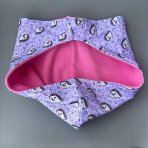 May include: A pink and purple hooded scarf with a hedgehog print. The scarf is reversible and has a soft fleece lining.