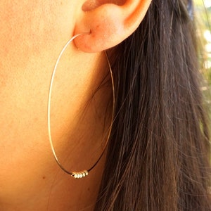 Peut inclure: Boucles d'oreilles créoles en or avec un petit groupe de perles dorées en bas.
