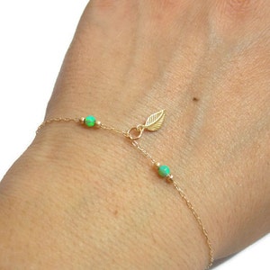 May include: A delicate gold chain bracelet with a small leaf charm and three green opal beads.