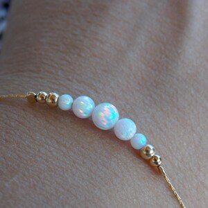 May include: A delicate gold chain bracelet with a row of white opal beads. The bracelet is on a person's wrist.
