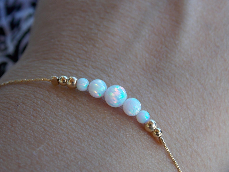 May include: A delicate gold chain bracelet with a row of white opal beads. The bracelet is on a person's wrist.