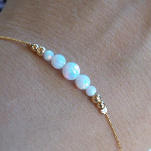 May include: A delicate gold chain bracelet with white opal beads. The bracelet is made with a simple design and features a subtle shimmer.
