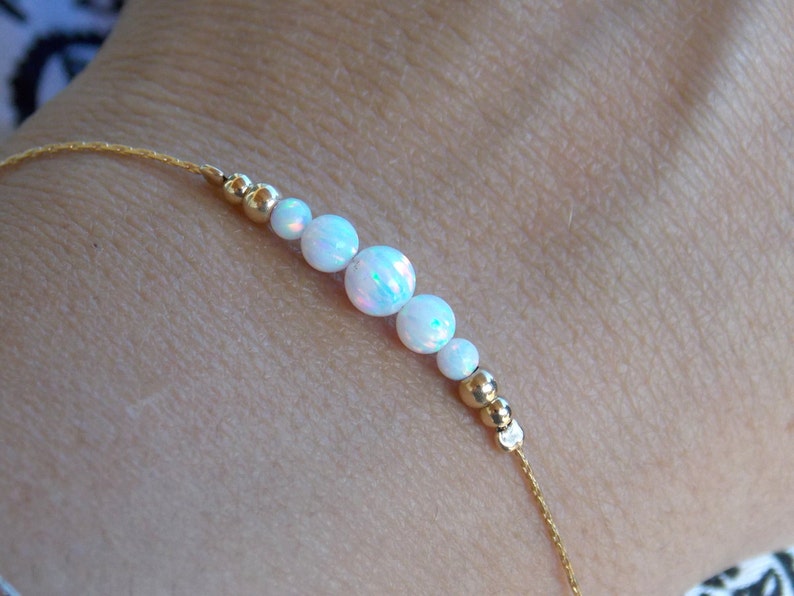May include: A delicate gold chain bracelet with white opal beads. The bracelet is made with a simple design and features a subtle shimmer.