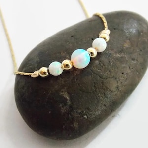Pu&ograve; includere: Una delicata collana a catena d'oro con quattro perle di opale bianco. La collana &egrave; esposta su una roccia grigia.