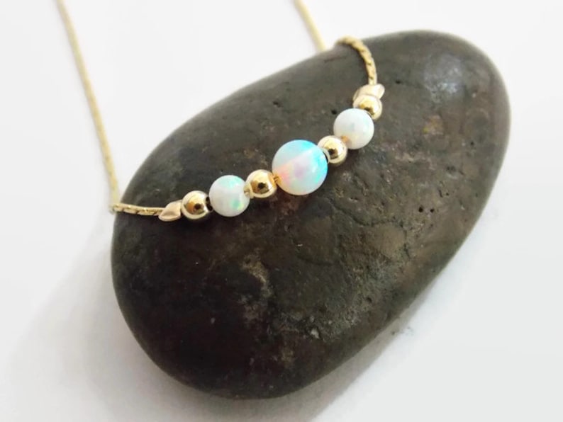 Pu&ograve; includere: Una delicata collana a catena d'oro con quattro perle di opale bianco. La collana &egrave; esposta su una roccia grigia.