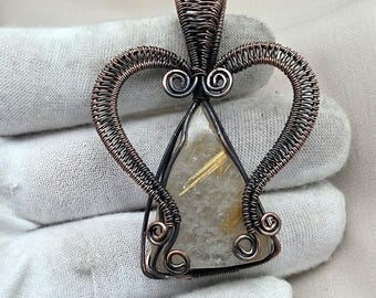 May include: A handcrafted pendant featuring a clear, triangular gemstone with golden inclusions, encased in intricate copper wire. The wirework forms a heart-shaped design with decorative swirls, creating a unique and artistic jewelry piece.