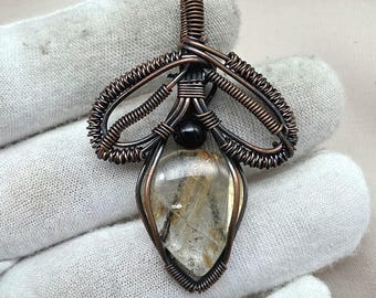 May include: A handcrafted pendant featuring a clear, teardrop-shaped gemstone with golden inclusions, encased in intricate copper wire. A small black bead accents the design. The pendant is suspended from a copper wire bail.